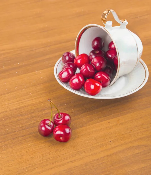 Сладкие вишни в белой чашке на деревянном столе с двумя вишнями — стоковое фото