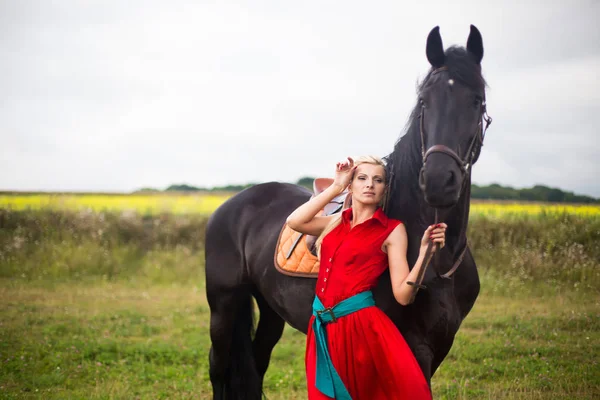 Mulher loira na moda montando um cavalo no dia ensolarado. Cabelo comprido . — Fotografia de Stock
