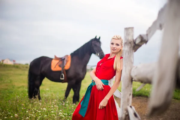 Schöne junge Frau in rotem Kleid mit Pferd im Freien — Stockfoto