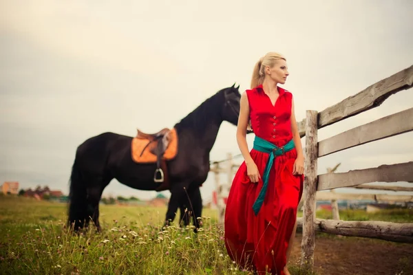 Bella giovane donna in abito rosso con un cavallo all'aperto — Foto Stock