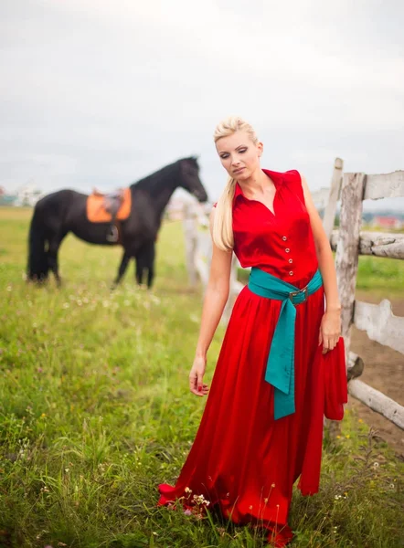 Mulher bonita em vestido vermelho com um cavalo ao ar livre — Fotografia de Stock