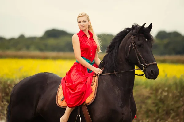 Modische blonde Frau, die an sonnigen Tagen ein Pferd reitet. lange Haare. — Stockfoto