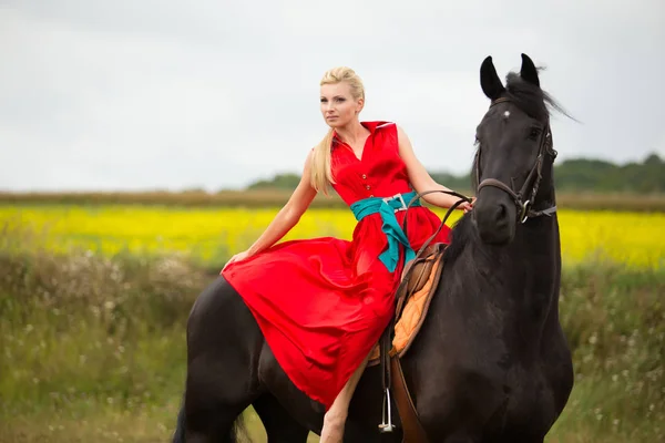 Modische blonde Frau, die an sonnigen Tagen ein Pferd reitet. lange Haare. — Stockfoto