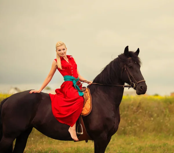 Mulher loira na moda montando um cavalo no dia ensolarado. Cabelo comprido . — Fotografia de Stock