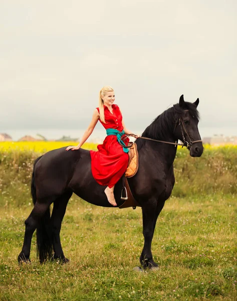 Modische blonde Frau, die an sonnigen Tagen ein Pferd reitet. lange Haare. — Stockfoto