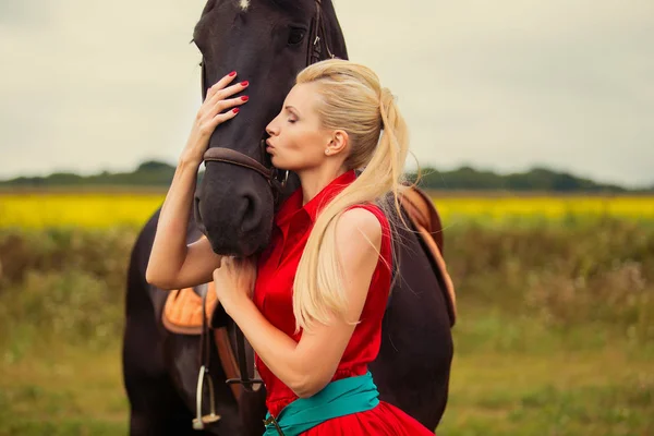 Modny blond kobieta na koniu w słoneczny dzień. Długie włosy. — Zdjęcie stockowe