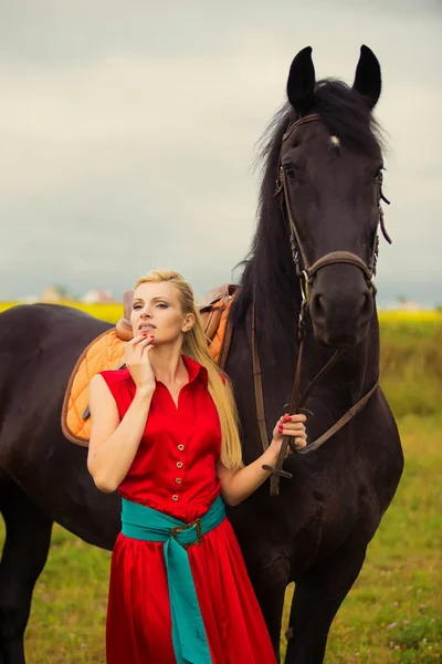 Modische blonde Frau, die an sonnigen Tagen ein Pferd reitet. lange Haare. — Stockfoto