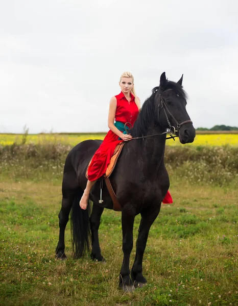 Fashionable blonde woman riding a horse in sunny day. Long hair. — Stock Photo, Image