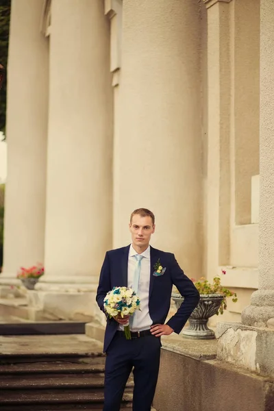 bir taş duvar ve col bir boquet ciddi damat duruyor