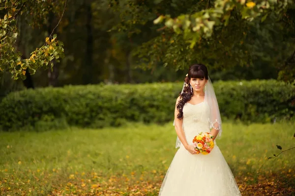 Bela noiva jovem de pé em um parque e sorrindo — Fotografia de Stock