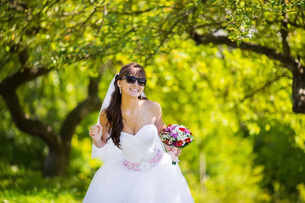 Beautiful bride in sunglasses posing in park — Stock Photo, Image
