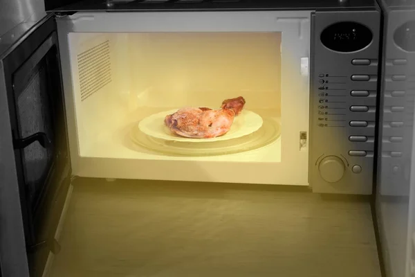 Πείνα το βράδυ. Θέρμανση πόδι κοτόπουλου στο φούρνο μικροκυμάτων — Φωτογραφία Αρχείου