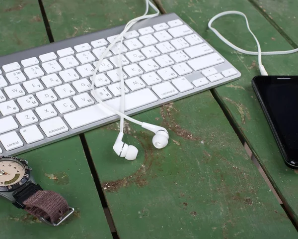 Tastatur, Smartphone, Uhren und Kopfhörer auf altem grünen Holz — Stockfoto