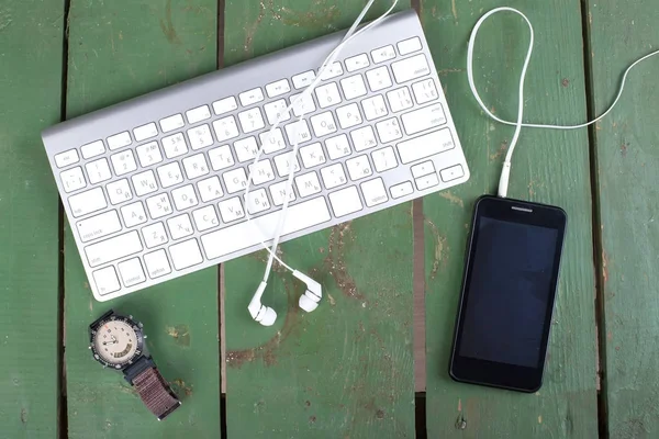 Teclado, telefone inteligente, relógios e fones de ouvido em madeira verde velha — Fotografia de Stock