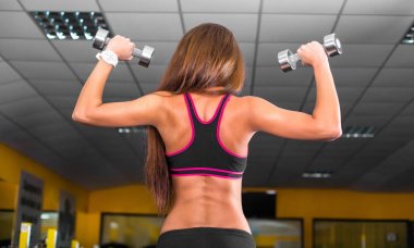 Güzel esmer kadın ağırlık kaldırıyor ve spor salonunda pazılarını çalıştırıyor.