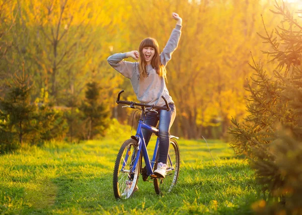 両手を自転車に広げており 夕暮れ時の緑の牧草地で ビューを探して幸せな女の子 — ストック写真