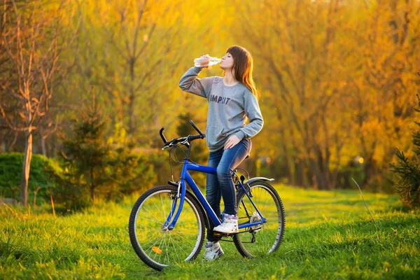 소녀는 음료수 병에서 일몰에 야외에서 자전거에 — 스톡 사진