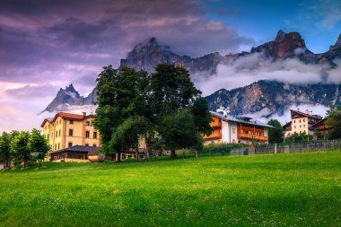 Günbatımında evleri ve yüksek dağları olan bir köy, Dolomitler, İtalya