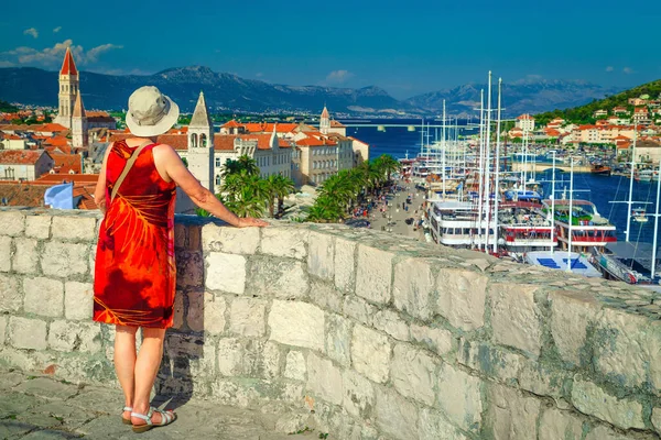 Attractive elderly woman with red dress and hat, enjoying the view from the Kamerlengo castle in Trogir, Dalmatia, Croatia, Europe