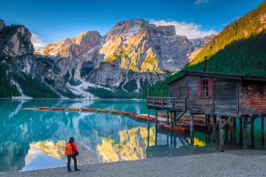 Sırt çantalı turist Braies Gölü kıyısının tadını çıkarıyor. Karlı dağları ve gölde ahşap botları olan resim gibi bir yer, Dolomitler, İtalya, Avrupa