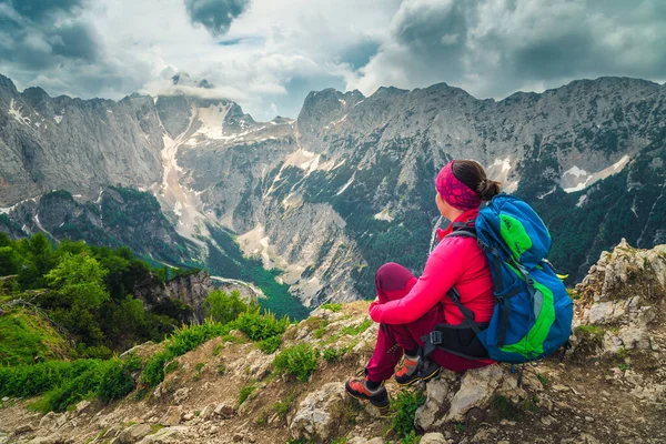 カラフルなバックパックを持つ陽気なハイカーの女性 スレメノバ スピカのハイキング スポット ジュリアン アルプス スロベニア ヨーロッパからの自由ハイカーの女性が座って ジャロヴェツの山のピークで景色を楽しんでいます — ストック写真