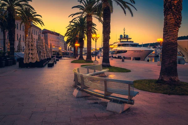 レストラン 観光港の通りのカフェと早朝の夜明けの街並み 港内の魅惑的なヨット トロギルのヤシの木や街路灯と美しい遊歩道の近く ダルマチア クロアチア ヨーロッパ — ストック写真