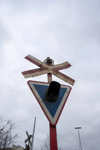 A rail road signal with one red light on. cloudy day