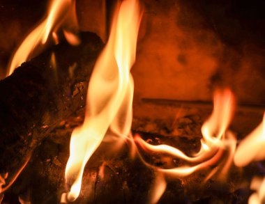 Alevler ve parlayan közle yanan bir şöminenin yanına.