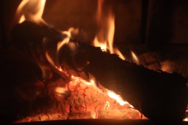 Alevler ve parlayan közle yanan bir şöminenin yanına.