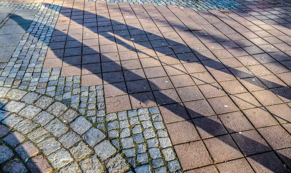 Shadows of people in a shopping area on a cobblestone ground