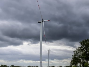 Rüzgâr türbinine yakından bak. Arka planda kara fırtına bulutlarıyla yenilenebilir enerji üretiyor.