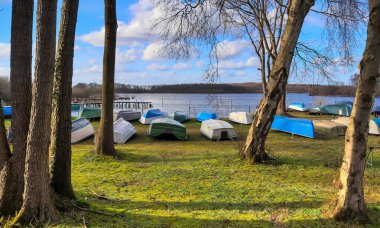 Güneşli bir günde, güzel bir gölün çimlerinde uzanan bir sürü kayık.