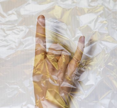 Plastik filme sarılı genç bir kadının elinde farklı semboller var.