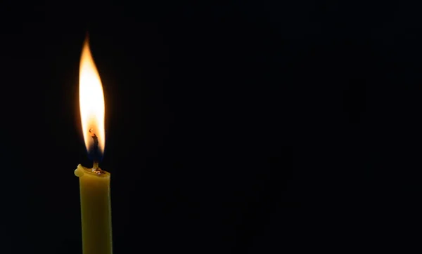 On a black background is a white flame of a wax candle. Concept - burning of life, religion, prayer. Copy space