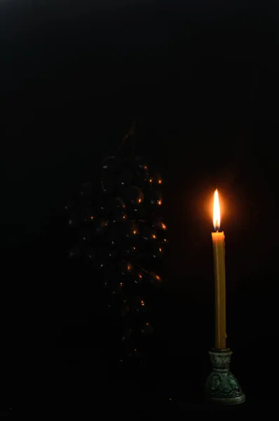 在黑色的背景上 有一把葡萄刷子 近处是燃烧的蜡烛 烛焰照亮了葡萄 平安夜 — 图库照片#