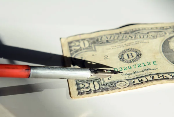 The pen of a red vintage pen fits into the signature on a twenty-dollar bill. Concept - fake money, business, deal