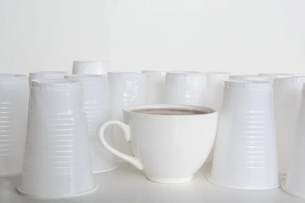 On a white background are white platonic cups. Among them is a ceramic cup. Concept - the fight against plastic pollution of the planet, the choice of natural materials