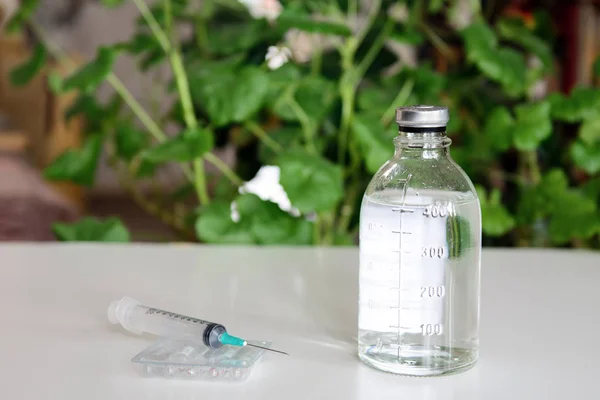 Against the background of plants, there is a bottle with a medical solution and a syringe with ampoules. Concept - health care, vaccination, protection against coronovirus
