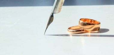 Beyaz arka planda iki alyans var. Gölgesi olan eski bir kalemin tüyünün yanında. Konsept - Nişan günü, aşk, sadakat