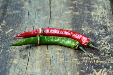 Eski tahtada yeşil ve kırmızı biberler birbirine itilmiş. Her biri alyans takıyor. Kavram - aile sevgisi, arkadaşlık