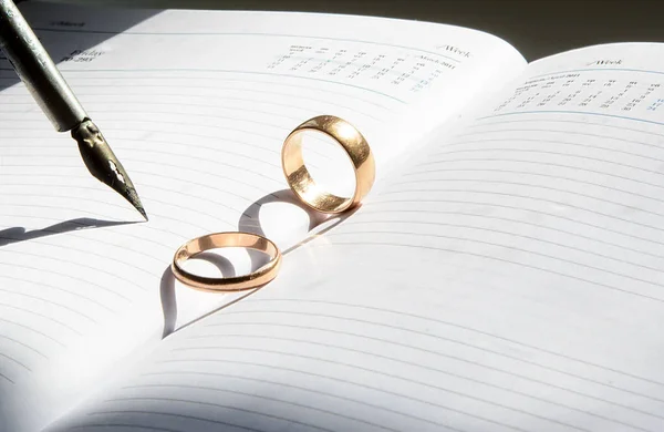 在开放的周报上有两个圆环 它们产生了心形的阴影 靠近羽毛复古钢笔 有阴影 订婚日 — 图库照片