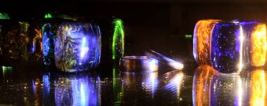 Siyah bir zemin üzerinde, renkli kristaller - yeşil, mavi, turuncu parlak ışıkla aydınlatılmış. Ayna. Neon ışığı. - Evet. Kristallerin arka planında, altın alyanslar. Konsept - Düğün ayini, nişan