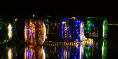 Karanlıkta parlak ışıkla aydınlatılan renkli kristaller arasında altın bir zincir. Konsept - lüks, değerli arka plan,