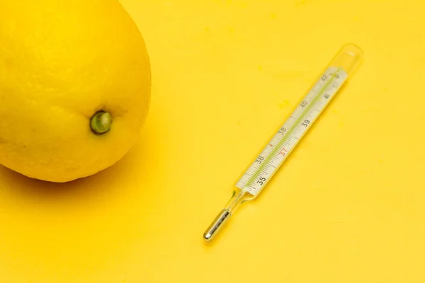 黄色背景上有一个温度计和一个柠檬 豁免支助 — 图库照片