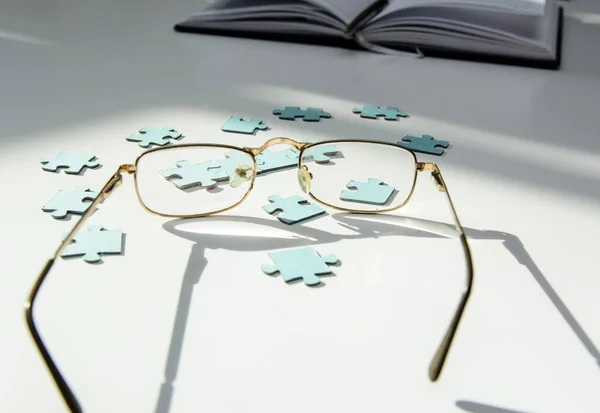 On a white background blue puzzles. Puzzles are visible through the glasses in gold frames. In the background is a weekly. Concept - leader selection, team, coronovirus test, patient identification