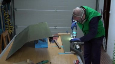 Yüzünde ve ellerinde koruma olan uzman bir işçi karbon fiber parçası kesme makinesiyle çelik yelek kesiyor ve atölyedeki tozu süpürüyor. Yarış arabası için üretim bölümü