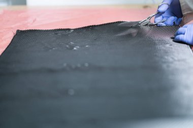 Eldivenlerle korunan ve karbon fiber kesen eller.