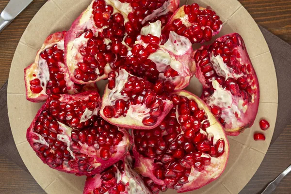 Healthy food. Pieces of ripe pomegranate with juicy grains on a disposable cardboard plate. Food photo, horizontal orientation. Vitamins and healthy trace elements from fruits