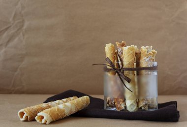 El yapımı waffle tüpleri cam bir vazoda duruyor, arka planda el işi kağıt üzerine pudra şekeri serpiştirilmiş.