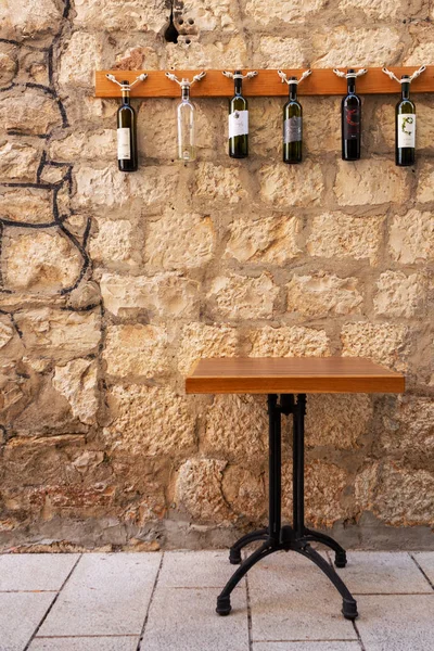 Een smeedijzeren tafel staat niet tegen de achtergrond van een prachtige, getextureerde oude muur gemaakt van grote steen en versierd met wijnflessen in een smalle straat van de oude Europese stad. — Stockfoto